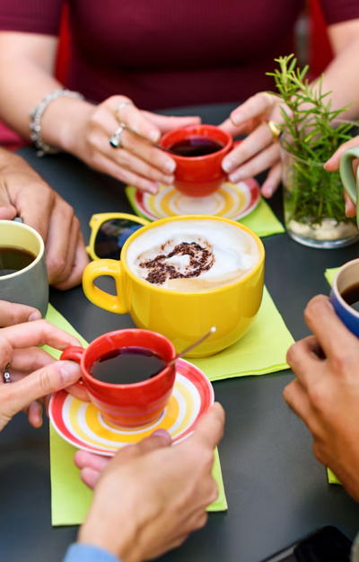 A group of people gathers around a table, enjoying colorful cups of coffee and conversation, creating a warm and inviting atmosphere.